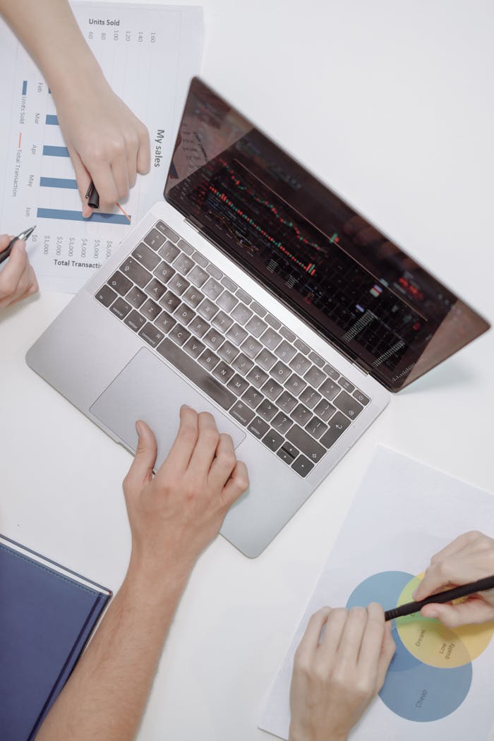 High-angle view of teamwork using a laptop and discussing financial charts in an office setting.
